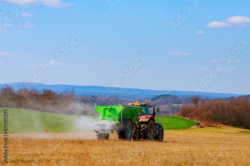 Fotografie The tractor spreads granular fertilizer on a grass field