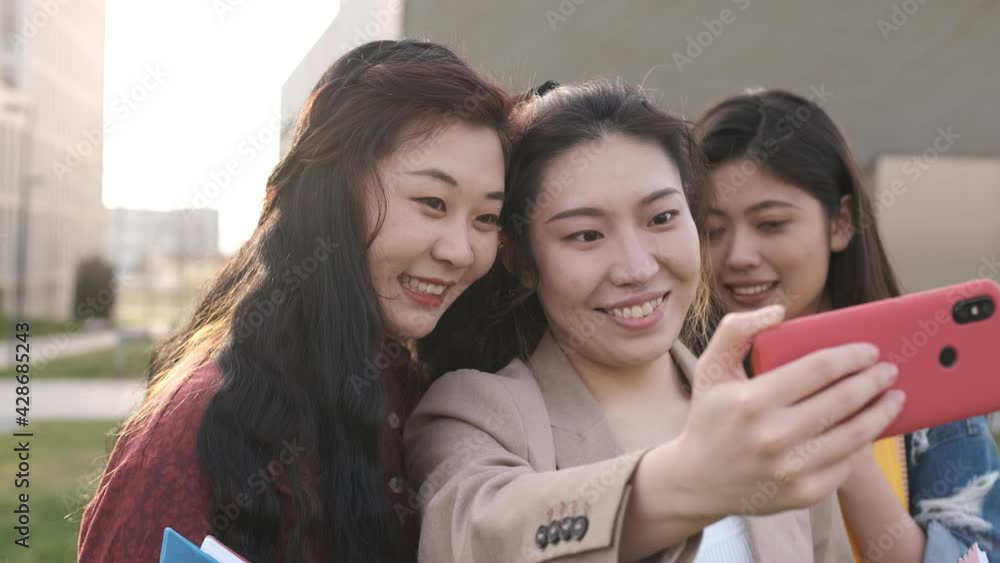 Asian college students taking a selfie with a mobile phone while standing outside the university campus. Education concept. Asian college students taking a selfie with a mobile phone while standing outside the university campus. Education concept.