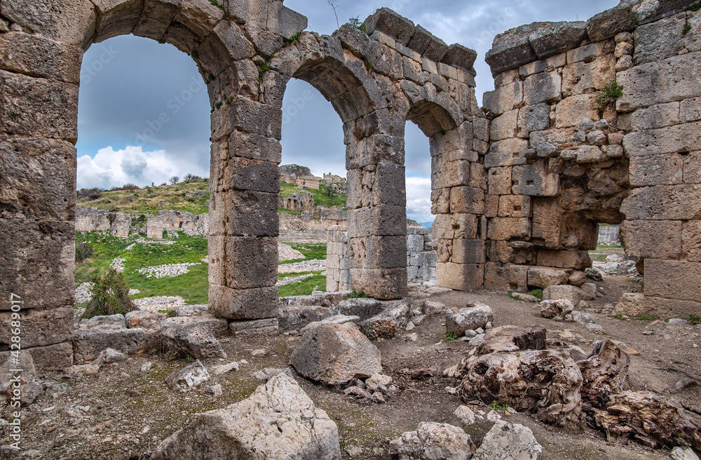 Tlos ruins, ancient Lycian hilltop citadel near the Seydikemer resort in the Mugla Province of southern Turkey. View of the Acropolis through the arches of small Roman baths in cloudy rainy weather.