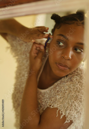 teenager in bantu knots looks into mirror while laying edges down