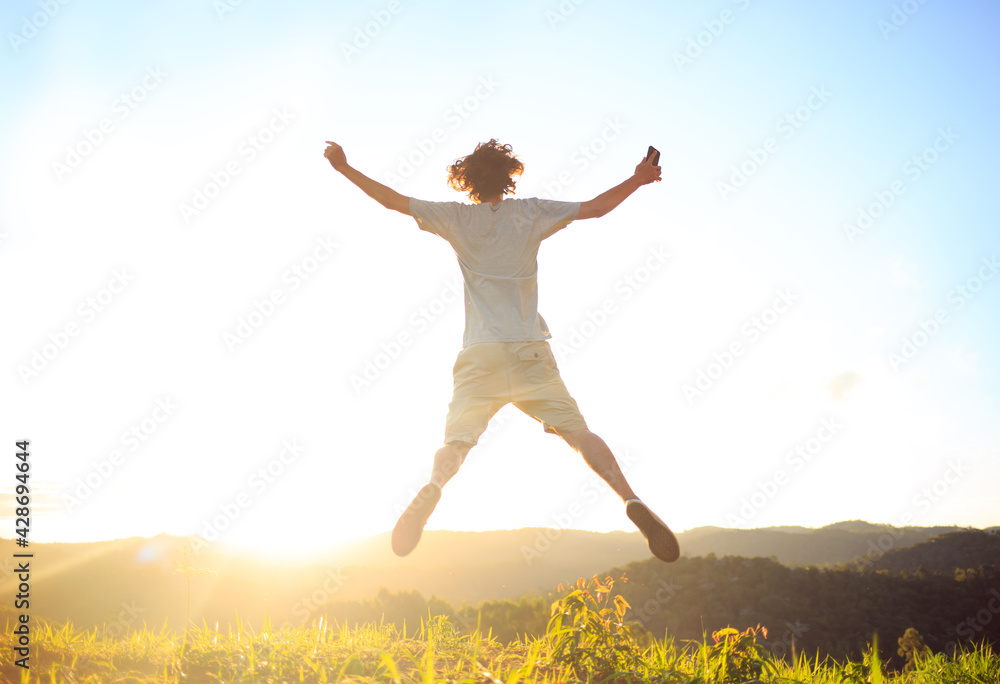 Man jumping and celebrating with arms raised with sunset in the background. Man jumping for joy, feeling happy and free.