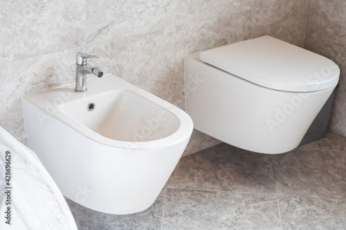 White wall-hung bidet and toilet on gray ceramic tiles in bathroom