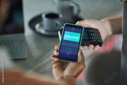 High angle closeup of African-American man paying via smartphone in cafe, copy space