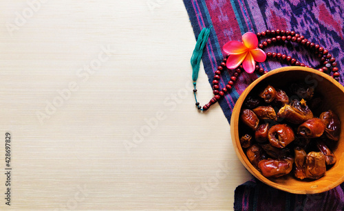 Ramadan background. Dates on wood bowl and prayer beads on cream background