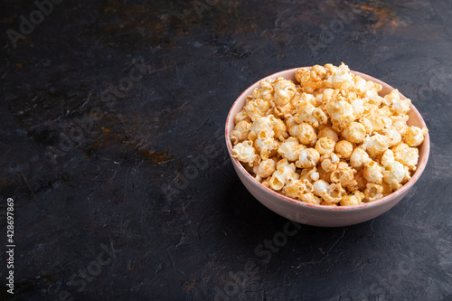 Popcorn with caramel in ceramic bowl on a black concrete background. Side view, copy space.