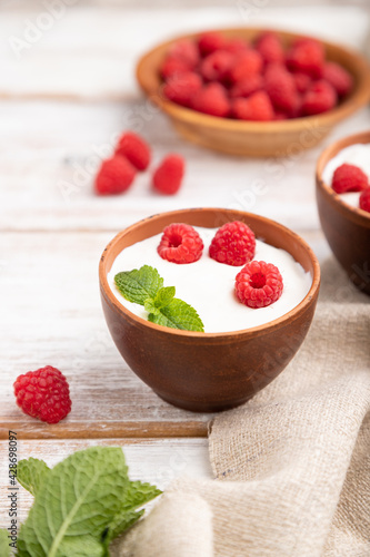 Yogurt with raspberry in clay cups on white wooden background. Side view, selective focus.