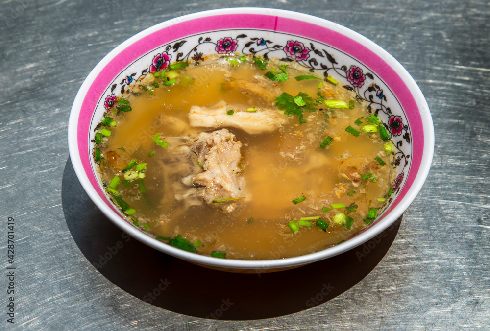 Hot clear soup of fresh pork rib seasoning with soy sauce and pepper. Pork bone soup in white bowl, Selective focus.