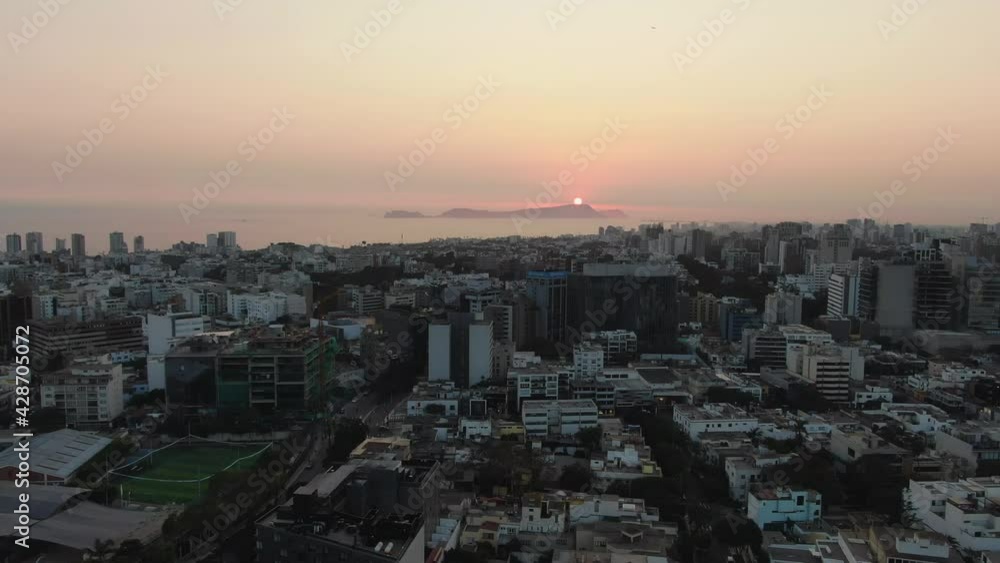 4k, aerial, dolly in, 30 fps, Video looking over the crowded Lima metropolis in Peru situated on the west coast at dawn, in the warm orange sunset lights falling over the waters of the Pacific Ocean. 4k, aerial, dolly in, 30 fps, Video looking over the crowded Lima metropolis in Peru situated on the west coast at dawn, in the warm orange sunset lights falling over the waters of the Pacific Ocean.