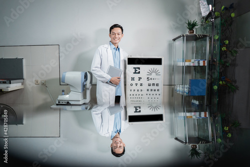 a male doctor posing next to an eye test kit located in an examination room at the eye clinic photo