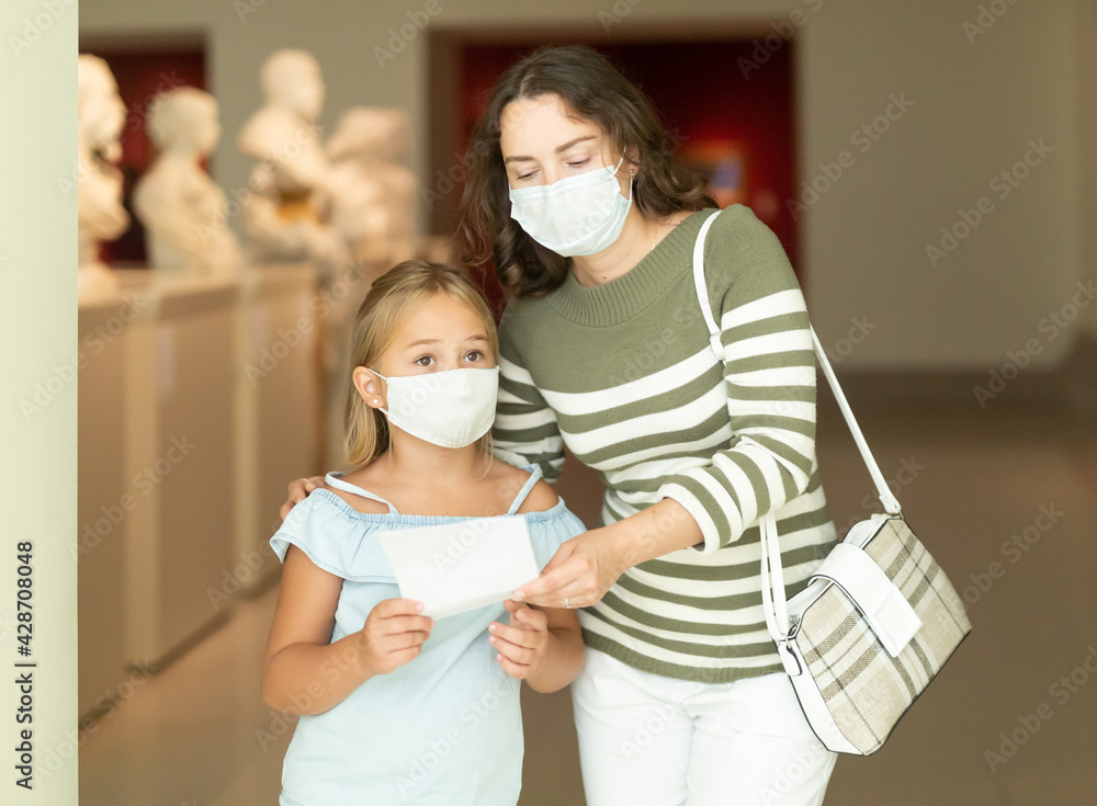 Young woman visitor with daughter looking at exhibition in museum of ancient sculpture ..