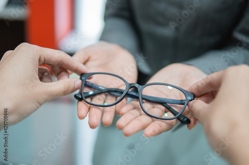 a shop assistant's hand gives a pair of glasses to the hand of a customer in an optician