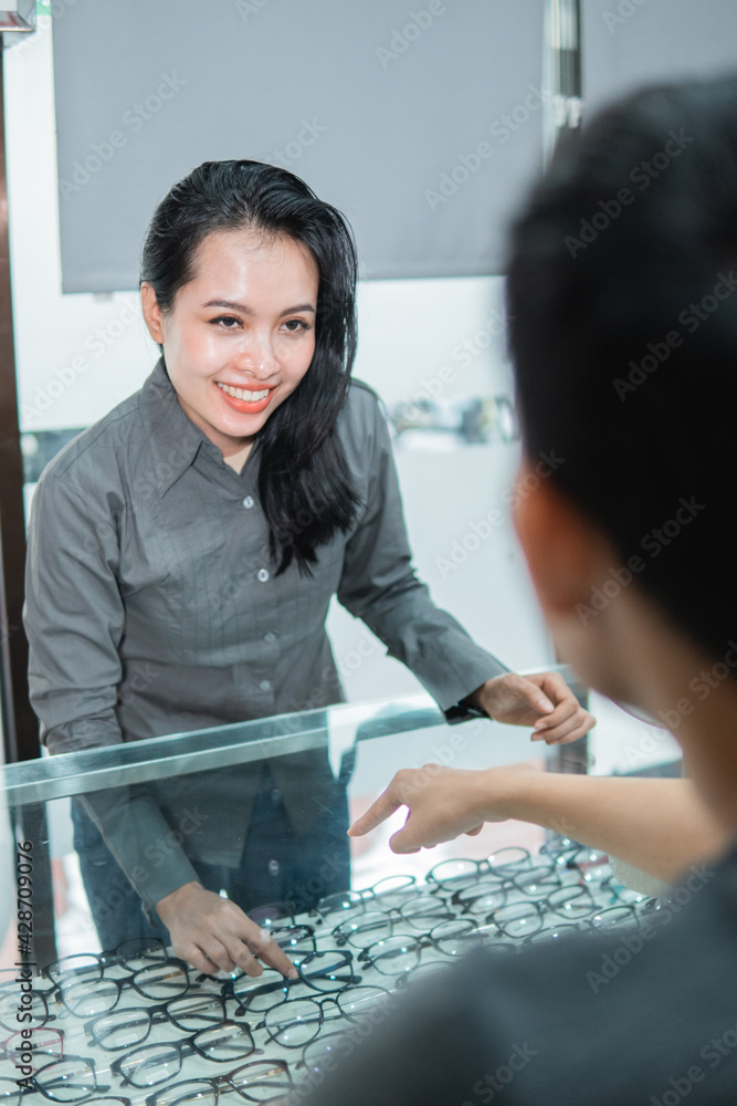 a shop assistant shows a pair of glasses in the window to a customer at an optician a shop assistant shows a pair of glasses in the window to a customer at an optician
