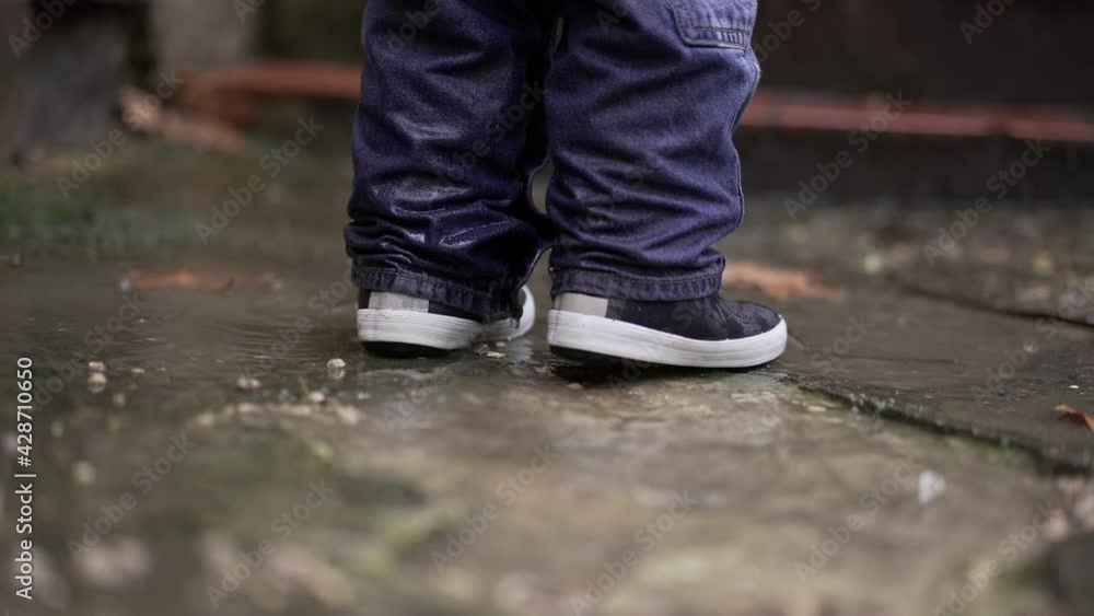 Toddler boy splashes into puddle of water. Child plays with puddles Toddler boy splashes into puddle of water. Child plays with puddles