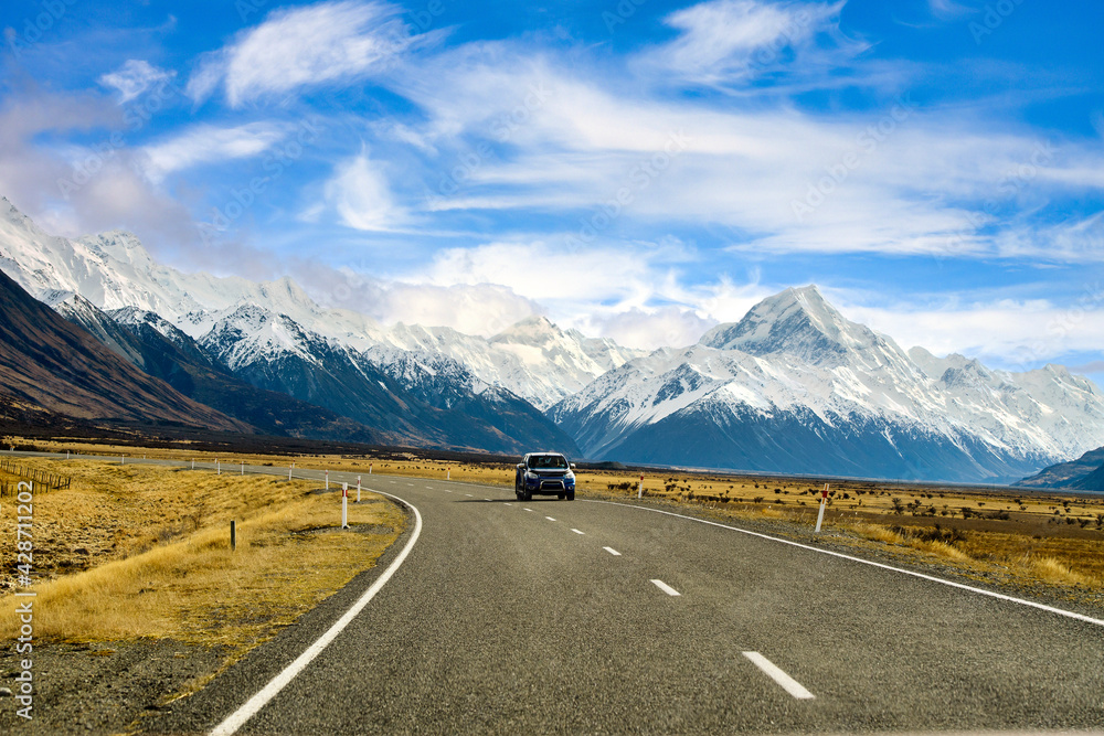 One car on the asphalt road to the big and tall Mountains in winter, dry grass turns yellow in blue skies and beautiful clouds in the daytime in New Zealand National Parks.