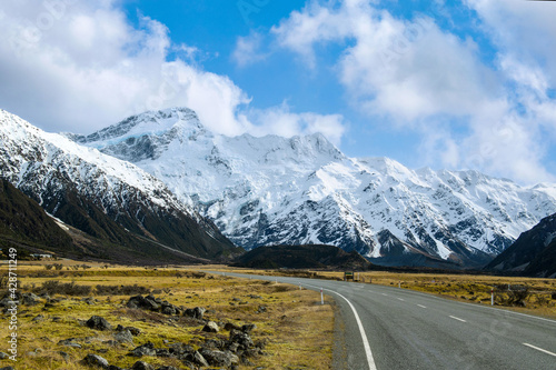 On the asphalt road to the big and tall Mountains in winter, dry grass turns yellow in blue skies and beautiful clouds in the daytime in New Zealand National Parks.