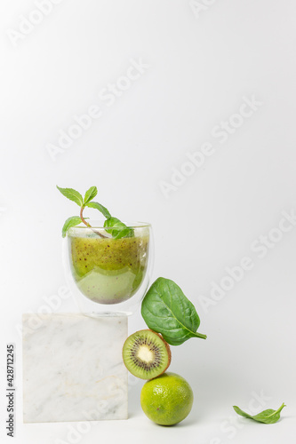 The concept of a detox cocktail of fruits and vegetables. Smoothie with kiwi, mint, lime and spinach on a stand over a white background. Vertically, copy space