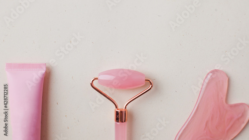 Fototapeta Naklejka Na Ścianę i Meble -  Rose quartz guasha stone, jade roller and pink tube with a moisturizing cosmetic product for the face. Skin care