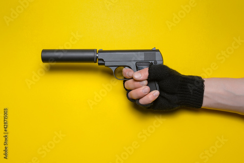 A toy pistol with a silencer in the male hand isolated on yellow background. photo