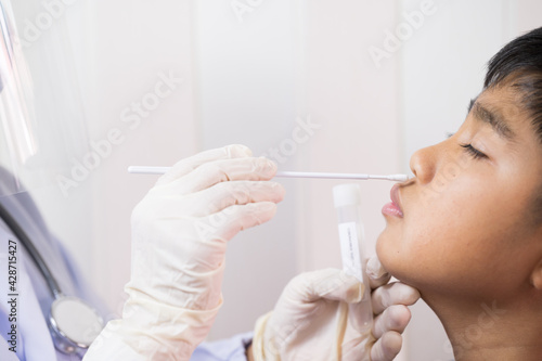 Doctor taking a swab for corona virus sample from potentially infected Asian boy nose.Covid-19 laboratory test.Medical staff with PPE suit test coronavirus  to asian kid by nose swab at hospital.