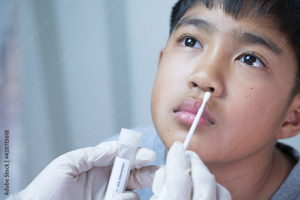 Doctor taking a swab for corona virus sample from potentially infected Asian boy nose.Covid-19 laboratory test.Medical staff with PPE suit test coronavirus to asian kid by nose swab at hospital. Doctor taking a swab for corona virus sample from potentially infected Asian boy nose.Covid-19 laboratory test.Medical staff with PPE suit test coronavirus to asian kid by nose swab at hospital.