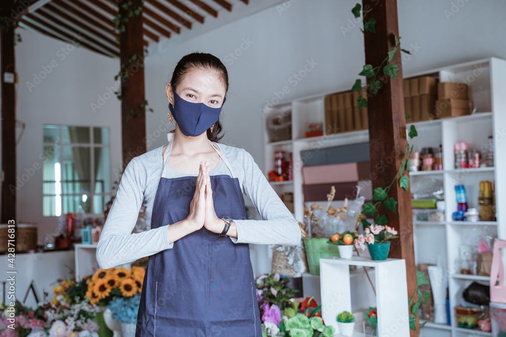 young woman manager wearing apron and face mask florist standing pose greeting welcome looking camera