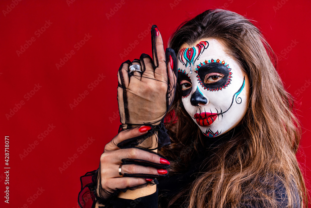 mexican young woman in a costume of Calavera Catrina over red studio background