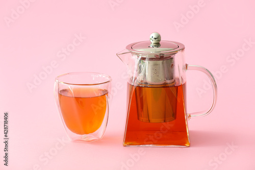 Teapot with hot tea and glass on color background