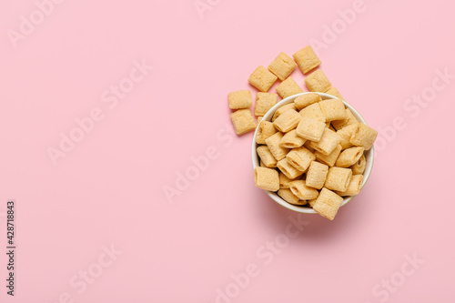 Bowl with tasty corn pillows on color background