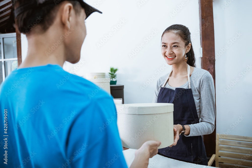 portrait courier smiling bring the package for young female shopkeeper receiving a package from courier