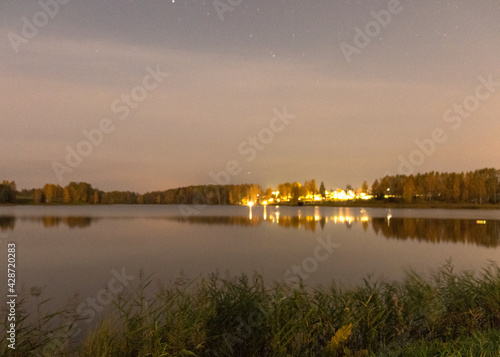 blurred wallpaper with lake at night, blurred lights on the horizon, lake reeds and grass in the foreground, autumn