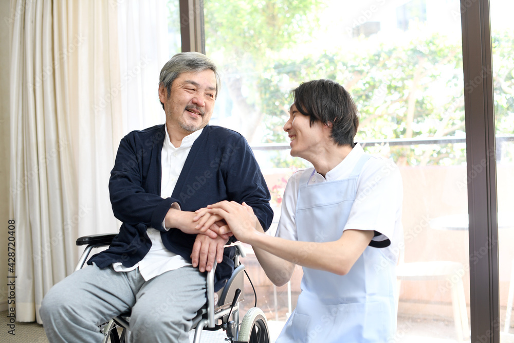 車椅子に乗る高齢者男性と寄り添う男性介護士