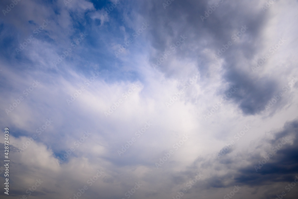 Stormy grey cloud with puffy white ones and blue sky. Horizontal cloudscape shot near horizon.