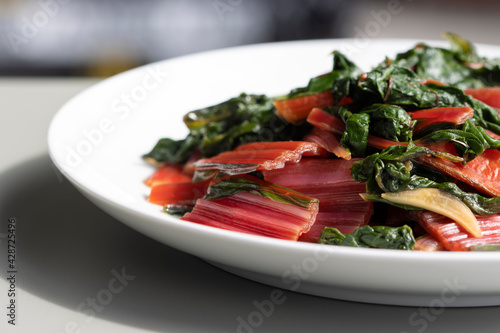 Closeup of sautéed red Swiss chard with garlic and lemon on a white plate. Selective focus. Swiss chard (also known simply as chard) is a leafy green vegetable that is related to beets and spinach.