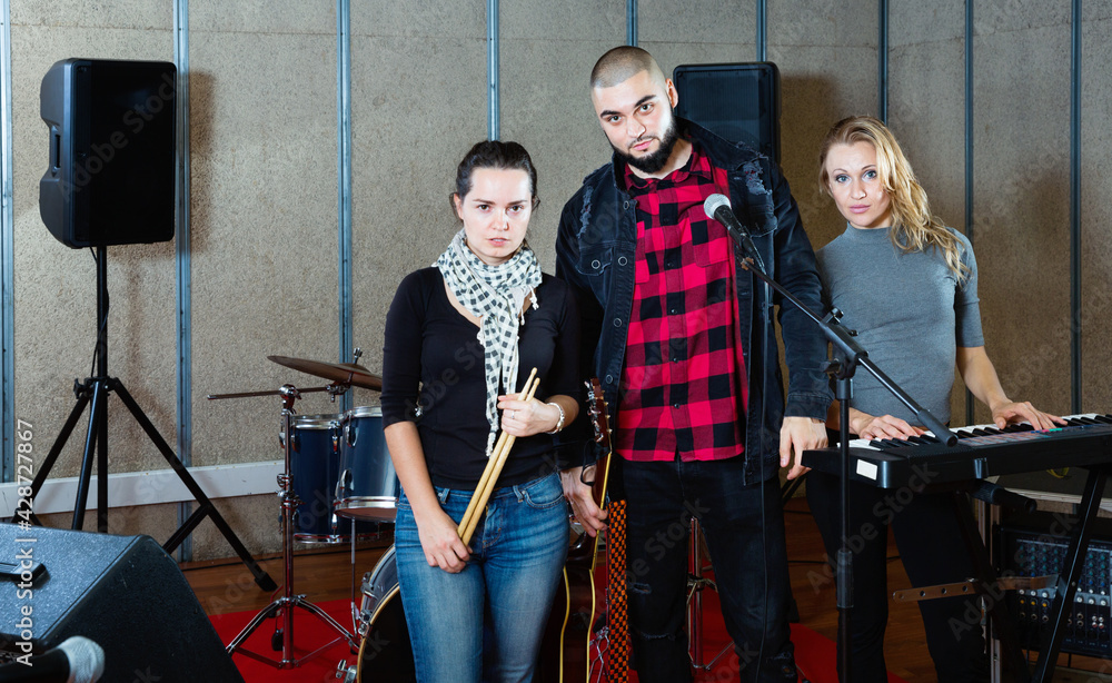 Three happy cheerful smiling bandmates posing together with musical instruments in rehearsal room
