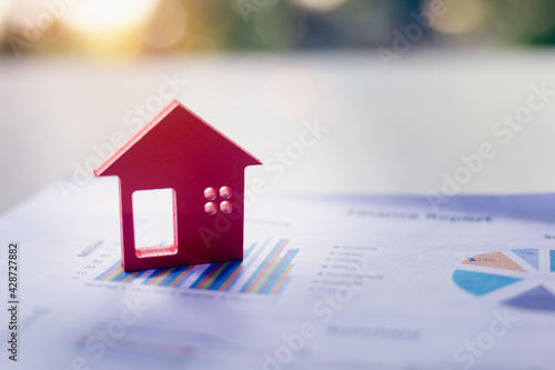 The red wooden house is placed on the graph or business information. Business growth concept. Economic chart. Real estate market. Mortgages. High profit home taxes for business investments.