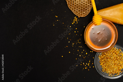 A ladle of honey on the background of a honeycomb of a bee. Honey tidbit in a glass jar honey spoon, bee bread and a honeycomb of wax on a black background. Healthy food concept.