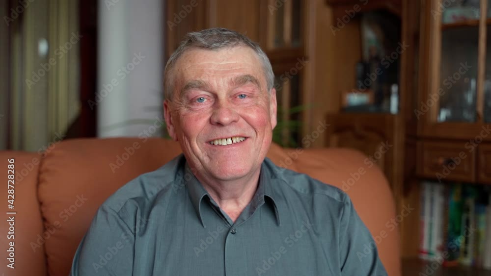 Happy elderly senior adult gray-haired 60s man smiling face healthy teeth sit on sofa. relaxed old retired single grandfather posing alone at home look at camera and smiling indoors, close up portrait Happy elderly senior adult gray-haired 60s man smiling face healthy teeth sit on sofa. relaxed old retired single grandfather posing alone at home look at camera and smiling indoors, close up portrait