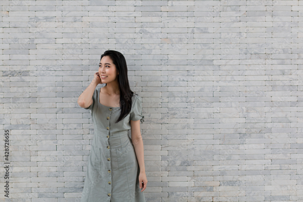 Portrait of a happy Asian girl in dress standing by the stone wall. Young traveling woman standing near stone wall during holiday. Tourist woman standing by the wall.