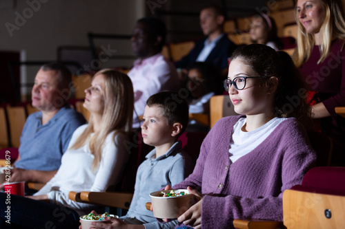Portrait of teen girl with family sitting in movie theater with popcorn and drinks, watching interesting film