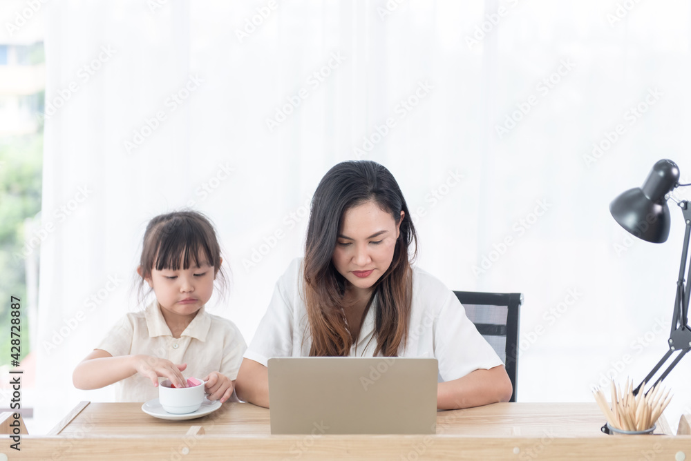 Asian young mother use computer notebook with little daughter sitting beside her at home Asian young mother use computer notebook with little daughter sitting beside her at home
