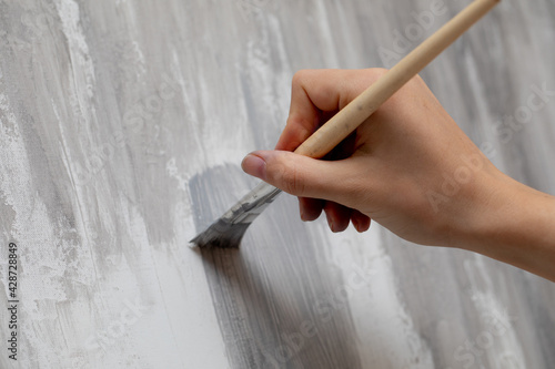 Abstract monochrome grey background, pattern in fancy design. Closeup of texture in white, gray and black brush strokes of acrylic paint. woman hand holds a brush covered by grey acrylic paint.