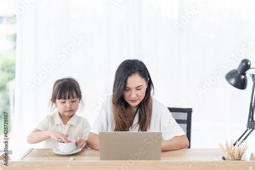  Asian young mother use computer notebook with little daughter sitting beside her at home