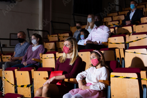 Mom and daughter in protective masks in auditorium watching play in the theater
