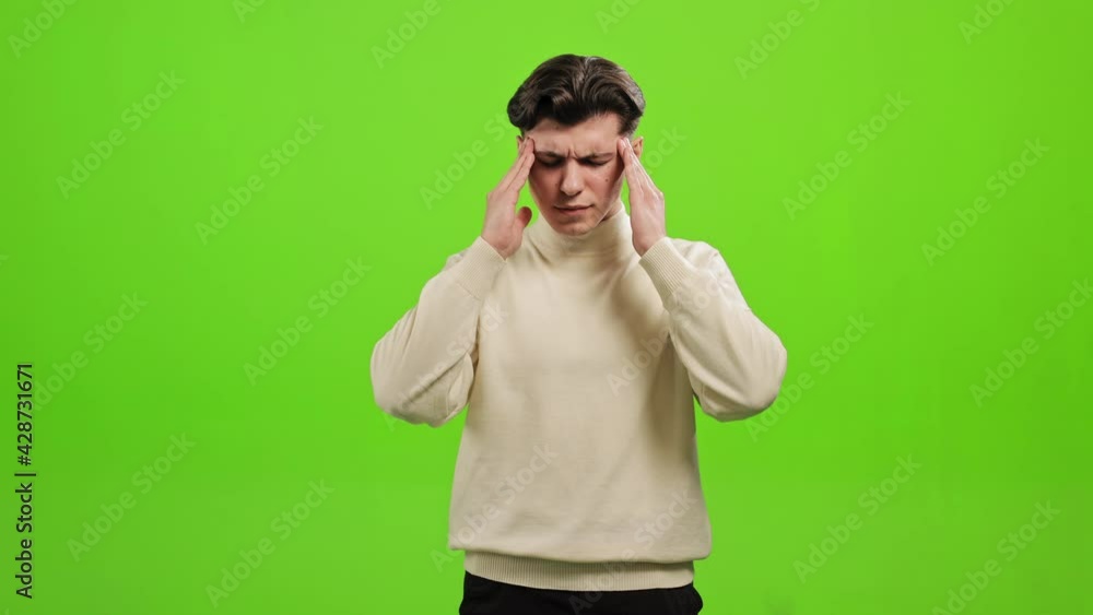 The man is standing and looking at the camera. He is raising his hands and holding his head. His head is hurting. He is standing on a green background. Green screen. 4K The man is standing and looking at the camera. He is raising his hands and holding his head. His head is hurting. He is standing on a green background. Green screen. 4K