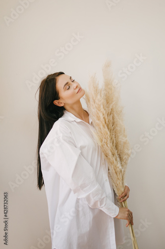 Young beautiful woman wearing white shirt standing with big bunch of pampass grass. photo