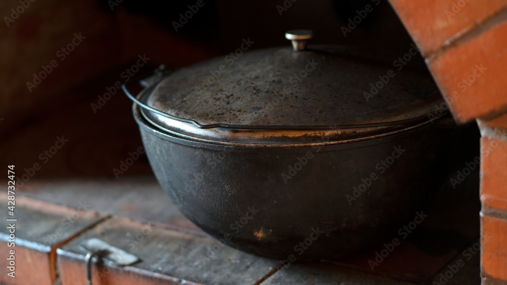 Cast-iron cauldron in rustic stove for cooking shurpa or pilaf. Village oven with an iron cooking surface. Cast-iron cauldron in rustic stove for cooking shurpa or pilaf. Village oven with an iron cooking surface.