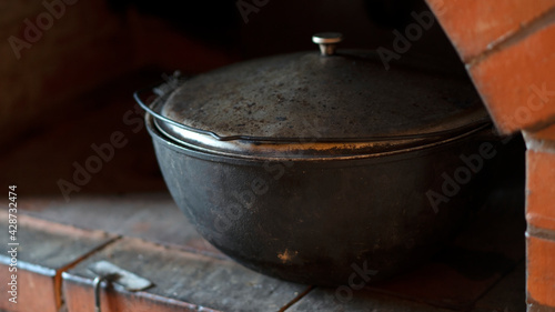 Cast-iron cauldron in rustic stove for cooking shurpa or pilaf. Village oven with an iron cooking surface. 