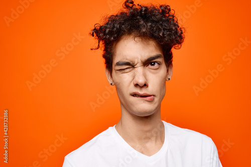cute guy in white t-shirt curly hair grimace orange background © SHOTPRIME STUDIO