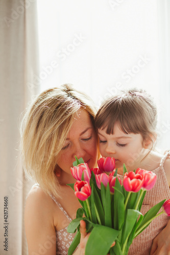 Little girl hugging her mother and sniffing tulips