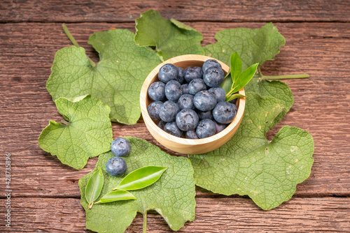 Fresh Blueberries on wooden tray with green leaves background.